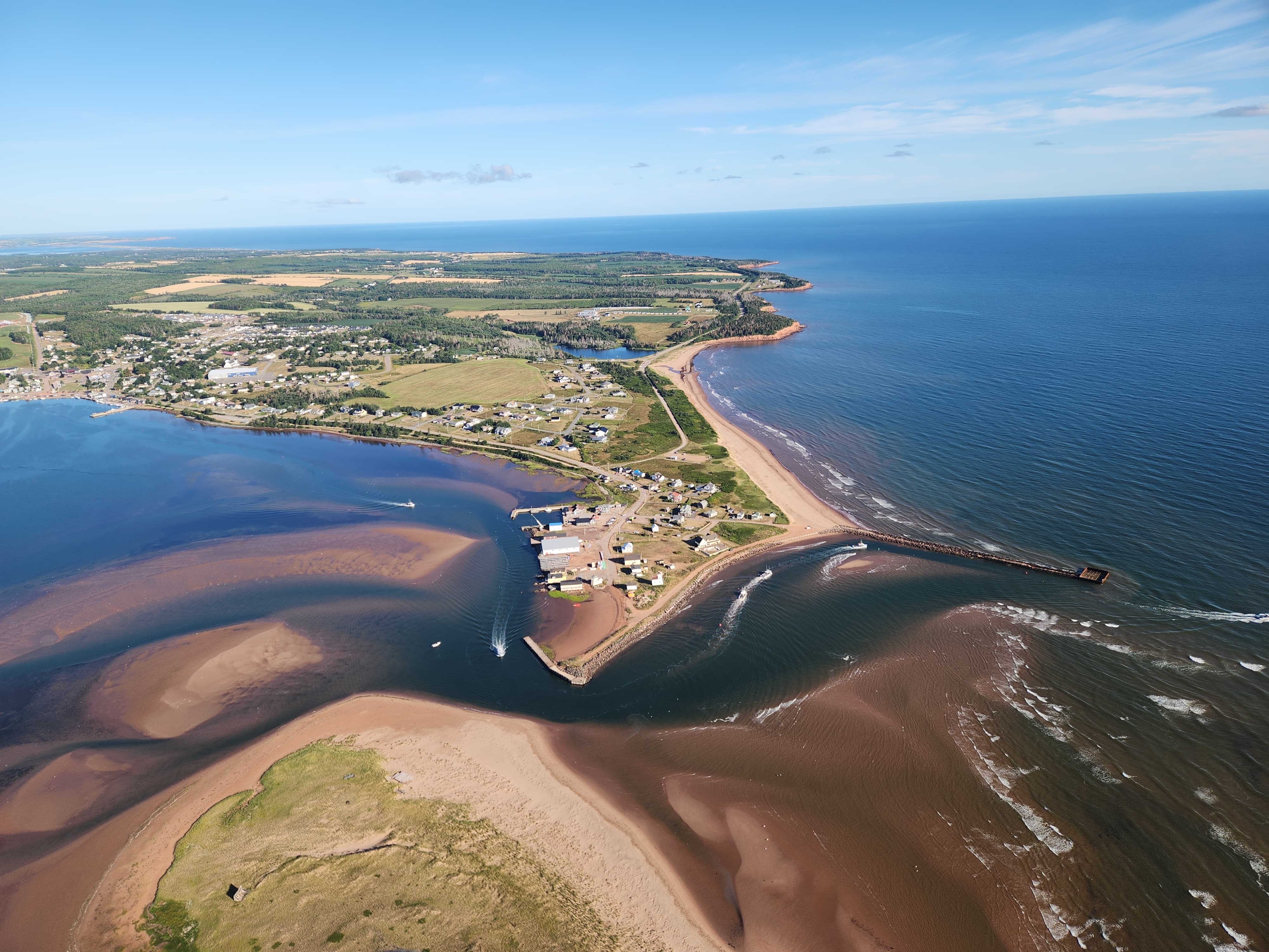 Aerial view of North Rustico Harbour showing the picturesque fishing village, protected harbour with colorful boats, red cliffs, and calm waters perfect for paddle boarding